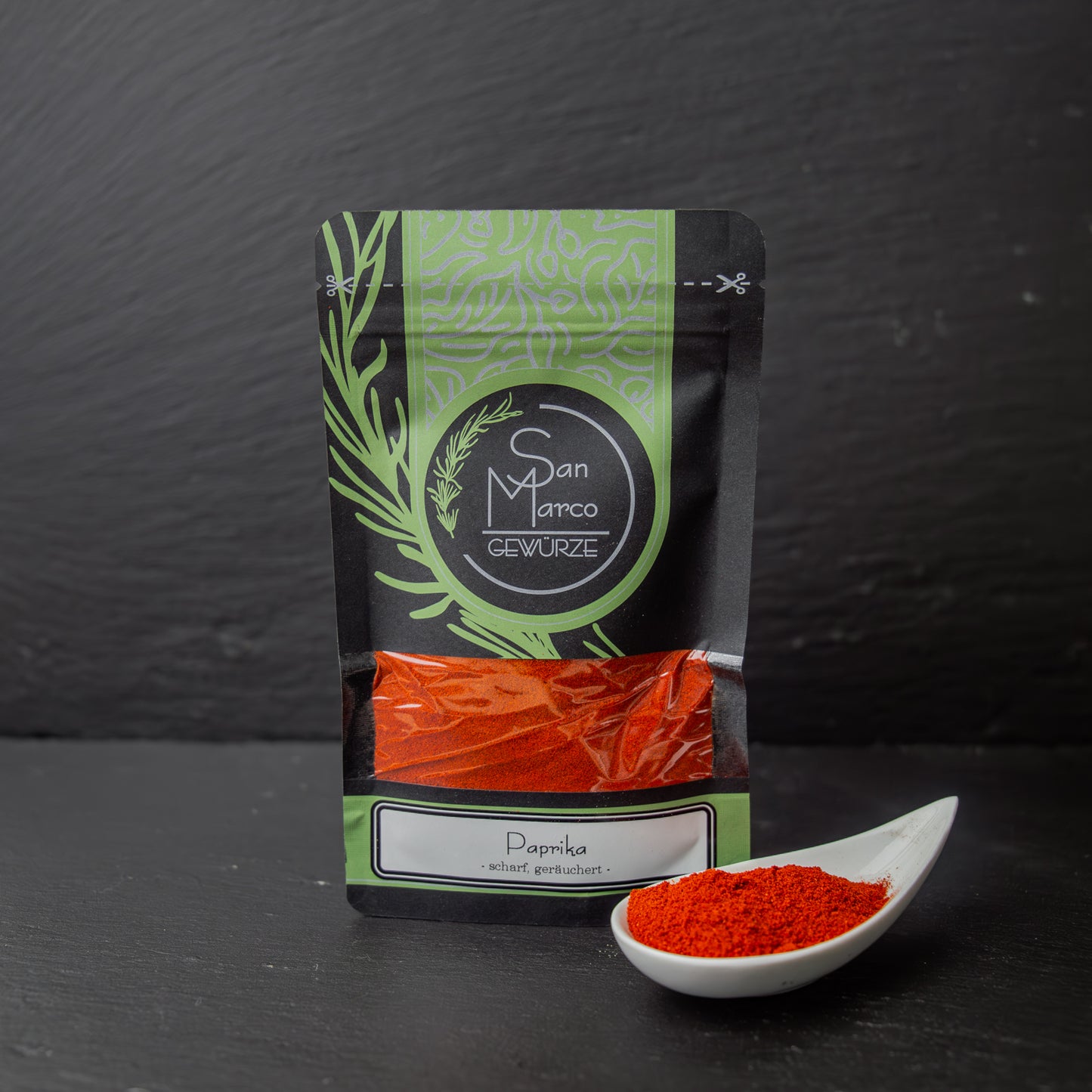 SanMarco Beutel Paprika geräuchert scharf neben weißer Schale mit tiefrotem Gewürzpulver