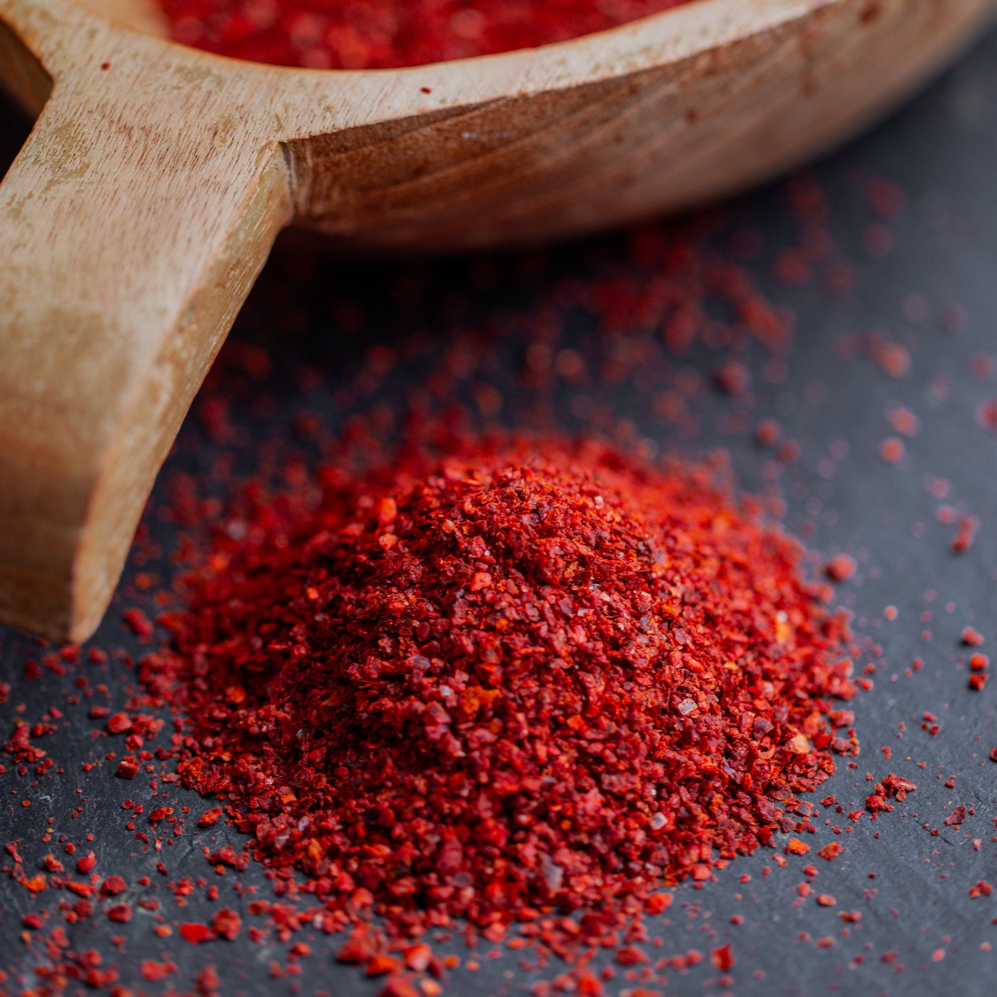 Paprikagranulat rot mit Saat auf dunklem Untergrund mit Holzlöffel