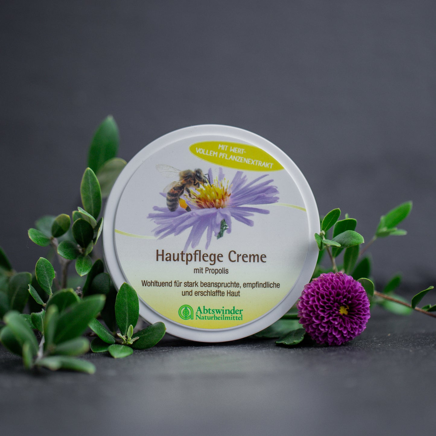 Propolis Creme auf dunklem Untergrund mit lila Blüte und grünblättrigem Zweig