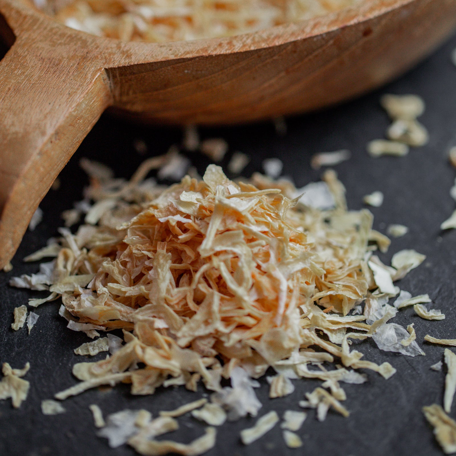 Zwiebelflocken auf dunklem Untergrund mit Holzlöffel